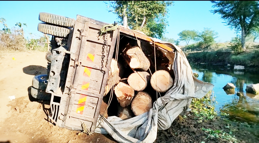 नदी किनारे लकड़ी से भरी वाहन पलटा